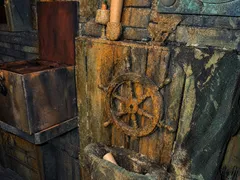 Steuerrad an einer bemoosten Holzwand, darunter ein Netz, daneben eine offene Truhe