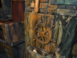 Steuerrad an einer bemoosten Holzwand, darunter ein Netz, daneben eine offene Truhe