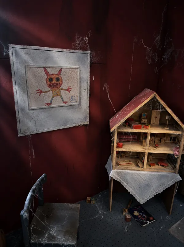 Puppenhaus vor der roten Wand, daneben die große Zeichnung eines kleinen Monsters