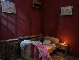 Kinderzimmer mit Bett, Nachttisch und Kinderzeichnungen an der roten Wand